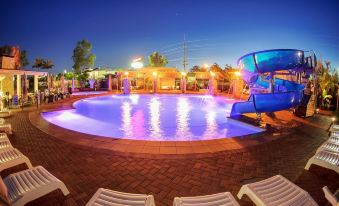 a large outdoor swimming pool with a water slide and lounge chairs is illuminated at night at Big4 Gold Coast Holiday Park