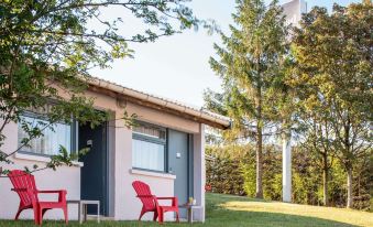 a red chair is placed in front of a house with a blue roof and trees nearby at Kyriad Lyon Est - Saint Quentin Fallavier