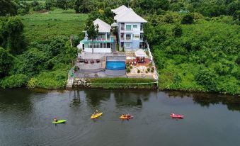 a group of people kayaking on a body of water , with a house in the background at Princess River Kwai Hotel