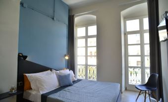 a bed with a blue headboard is in a room with arched windows and a small table at Habit