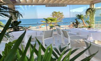 a patio area with a view of the ocean , featuring white chairs and potted plants at Mercure Villeneuve Loubet Plage