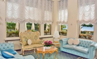 a luxurious living room with a blue and white color scheme , featuring a large window with curtains and a blue couch at Grand Hotel Menaggio