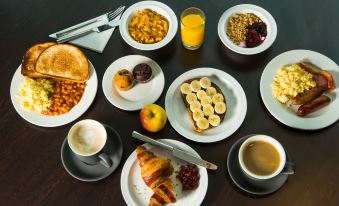 a table is filled with various breakfast items , including bread , fruit , and pastries , along with cups of coffee and juice at Holiday Inn Express Milton Keynes