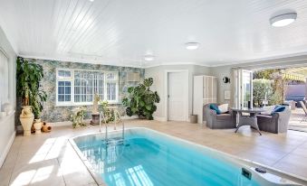 a modern swimming pool with a spacious living area , surrounded by large windows and plants at The Coast House B&B