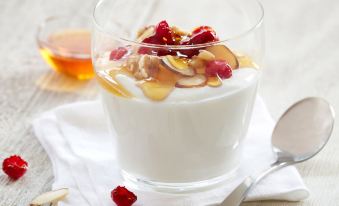 a glass of yogurt with fruit and nuts , served on a white plate , accompanied by a spoon and a cup of tea at Sonesta ES Suites Cincinnati - Sharonville West
