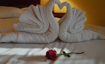 a bed with two white towels arranged in the shape of a swan , creating a romantic atmosphere at Golden Hotel