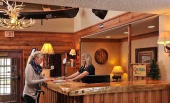 two women are working at a hotel reception desk , one of them is serving a customer at Boarders Inn & Suites by Cobblestone Hotels – Waukon