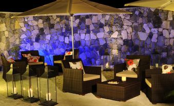 a patio area with a stone wall , lit by blue lights , and several chairs arranged around it at Constance Tekoma