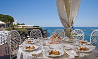 a table is set with plates , glasses , and a pitcher on an outdoor patio overlooking the ocean at Grand Hotel Baia Verde