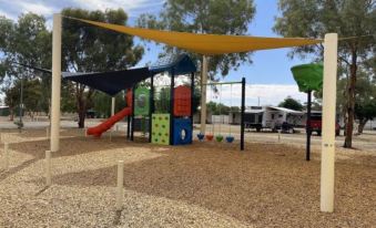 a playground with various play equipment , including slides , swings , and a slide bench , under a large yellow canopy at Broken Hill Tourist Park