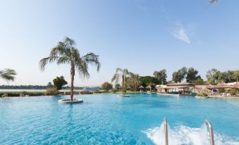 a large outdoor swimming pool surrounded by palm trees , with people enjoying their time in the water at Jolie Ville Hotel & Spa Kings Island Luxor
