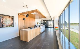 a modern , well - lit lobby with a long wooden counter and large windows offering views of the outdoors at Pacific Sands Apartments Mackay