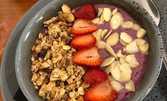 a bowl of yogurt with granola , strawberries , and almonds is placed on a wooden table at Motel Goolwa