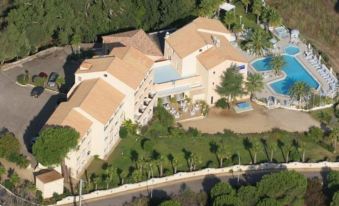 aerial view of a large building surrounded by trees and a pool , with a road in front of it at Hotel Corsica & Spa Serena