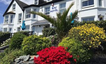 "a large white building with a sign that says "" bay hotel "" is surrounded by colorful flowers and bushes" at The Bay Hotel