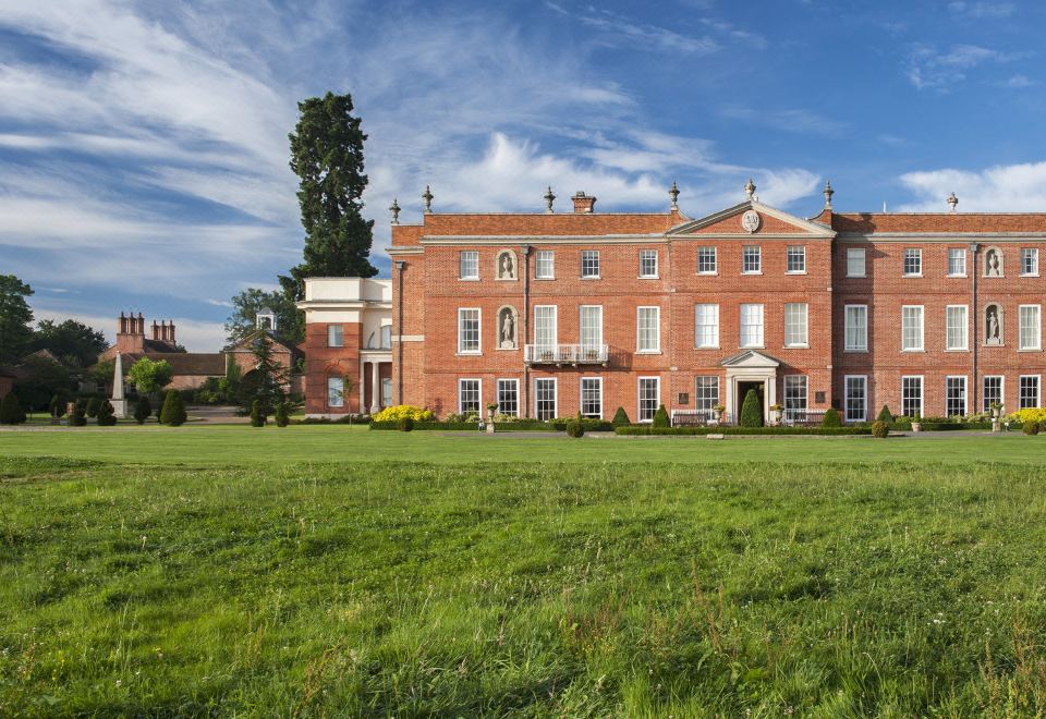 a large , red brick building surrounded by green grass and trees , with a blue sky in the background at Four Seasons Hotel Hampshire