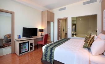 a modern hotel room with a large bed , tv , and desk , along with wooden flooring and white walls at Galaxy Hotel Banjarmasin
