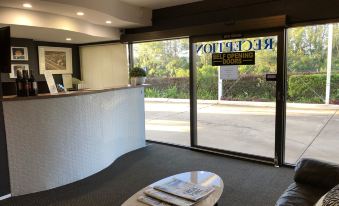 a hotel lobby with a reception desk , a coffee table , and a door leading to a car park at Logan City Motor Inn