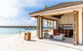 a wooden hut on a beach , surrounded by sand and water , with chairs and a table at Kagi Maldives Resort & Spa