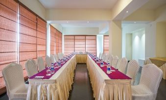 a long dining table with multiple chairs arranged around it , ready for a group of people to sit and eat at Hotel Grand Park Barishal