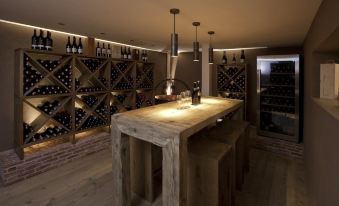 a wooden bar with a counter and wine bottles displayed on shelves behind it , illuminated by hanging lights at Hotel Hubertus - Au Bregenzerwald