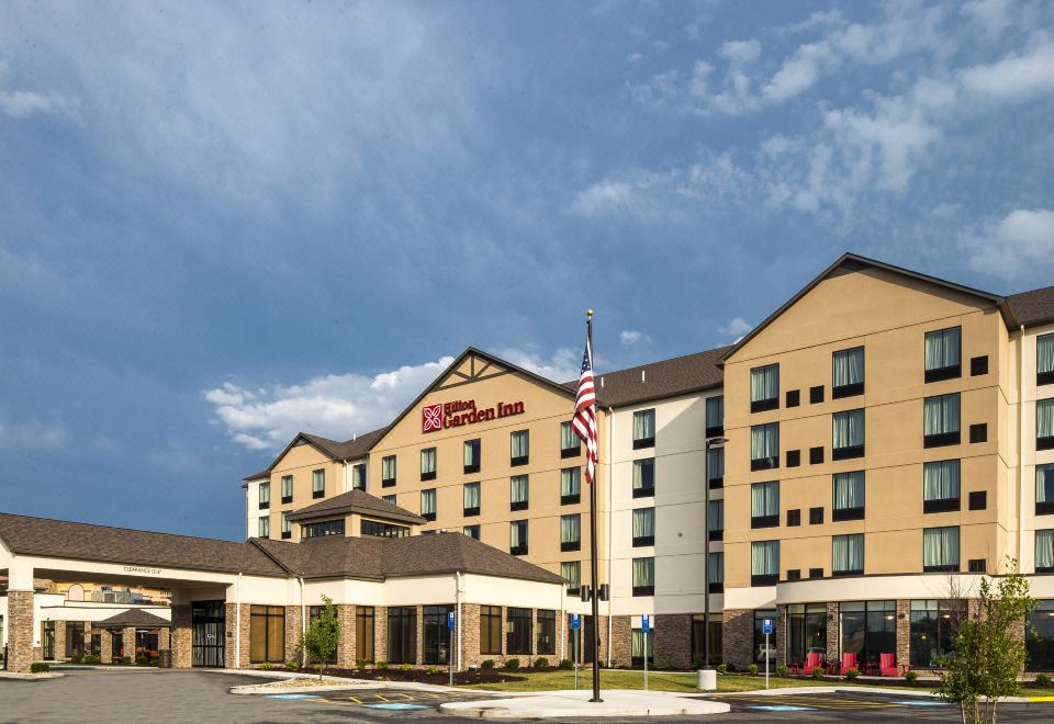 a large , modern hotel with an american flag on top , surrounded by a parking lot at Hilton Garden Inn Uniontown