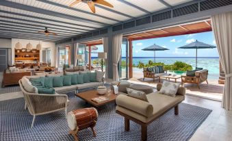 a modern , spacious living room with large windows offering views of the ocean and sky , featuring comfortable seating arrangements , wooden furniture , and an outdoor at Raffles Maldives Meradhoo Resort