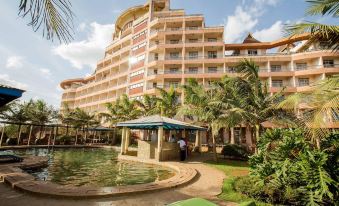 a large hotel with a pool surrounded by palm trees and a pond in front at Rainbow Ruiru Resort