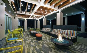 a modern outdoor lounge area with colorful seating , a fire pit , and wooden ceiling beams at Home2 Suites by Hilton Lawrenceville Atlanta Sugarloaf