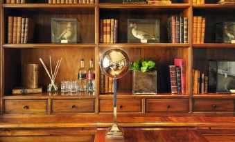 a wooden bookshelf filled with various books , a wooden shelf with a fan and a gold - colored object on top , and several glass vases at Rosewood Castiglion del Bosco
