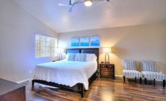 a modern bedroom with wooden flooring , white bedding , and a ceiling fan , along with two armchairs and a lamp at Arrowhead