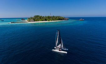 a sailboat is sailing in the ocean near an island , with a smaller island visible in the background at Outrigger Maldives Maafushivaru Resort