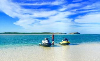 a person is standing on a sandy beach next to two jet skis , enjoying the view of the ocean at Pelican Beach Hotel