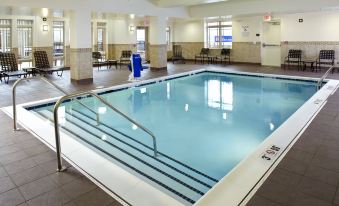 a large indoor swimming pool with a white tiled floor and blue water , surrounded by chairs and tables at HIlton Garden Inn Roanoke