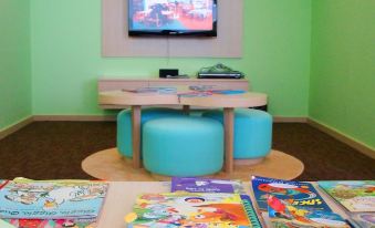 a children 's playroom with a flat screen tv , two blue ottomans , and several books arranged on the floor at Oakwood Premier Cozmo Jakarta