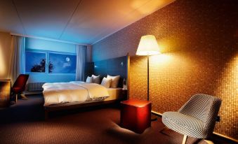 a cozy hotel room with a bed , nightstands , and a lamp , as well as a chair and stool in the corner at Pentahotel Wiesbaden
