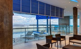 a modern , well - lit room with large windows offering an ocean view , surrounded by comfortable seating and a bar area at Cosmos Pacifico Hotel