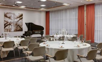 a dining room with a round table surrounded by chairs , and a piano in the background at Steigenberger Airport Hotel Amsterdam