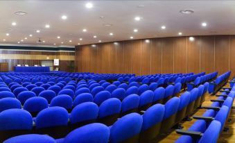 an empty auditorium with rows of blue chairs and wooden walls , under bright lights and large screens at Grand Hotel Salerno