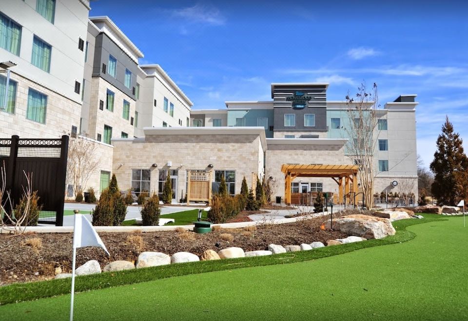 a modern hotel building with a large outdoor patio and lush greenery , under a clear blue sky at Homewood Suites by Hilton Hamilton