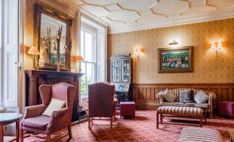 a cozy living room with wooden furniture , including a fireplace , chairs , and a couch , surrounded by elegant decorations at Makeney Hall Hotel