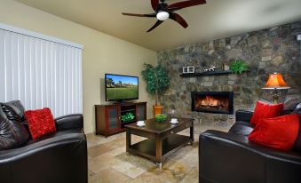 a living room with a stone fireplace , black leather couches , and a flat screen tv at Arrowhead