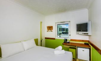 a hotel room with a green and white color scheme , featuring a double bed , a television , and a desk at Ibis Budget Brisbane Airport