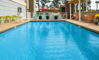 a large swimming pool with blue water and red umbrellas in a sunny outdoor setting at Home2 Suites by Hilton Lake City
