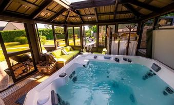 a large hot tub is situated in a room with a couch and chairs , surrounded by windows at La Ramade - Teritoria