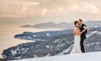 a couple is standing on a snow - covered hillside , embracing each other and posing for a wedding photo at Coyote Bluff Estate
