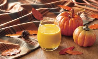 a glass of orange juice sits on a wooden table with pumpkins and leaves surrounding it at Comfort Hotel Koriyama