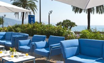 a row of blue chairs and a table with drinks on it in front of a beach at Hotel Victoria