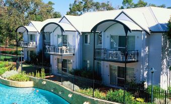 a row of three - story buildings with balconies and arched roofs are situated next to a swimming pool at Mandurah Quay Resort