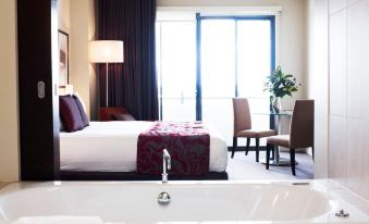 a hotel room with a large bed , a bathtub in the bathroom , and a view of a balcony at Rydges Campbelltown an EVT hotel